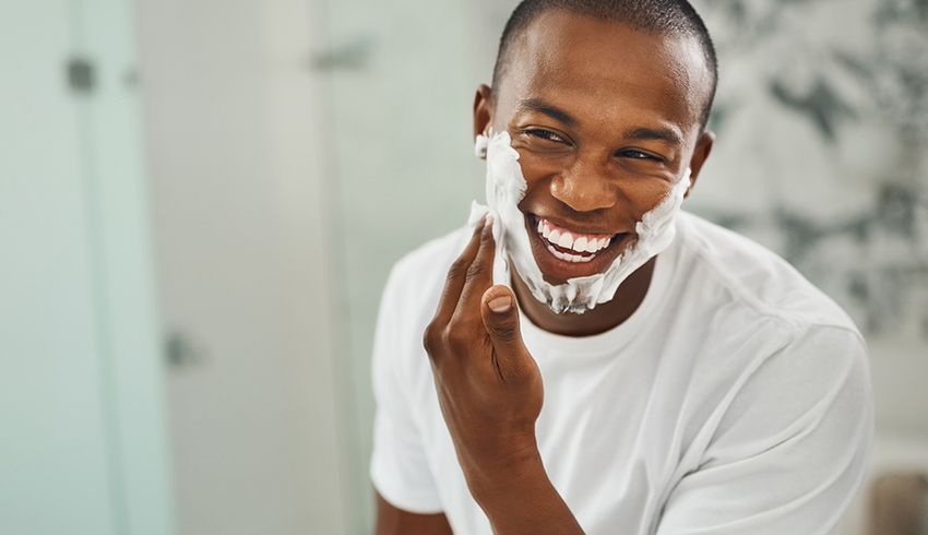 The reflection in a mirror of a man shaving his face.